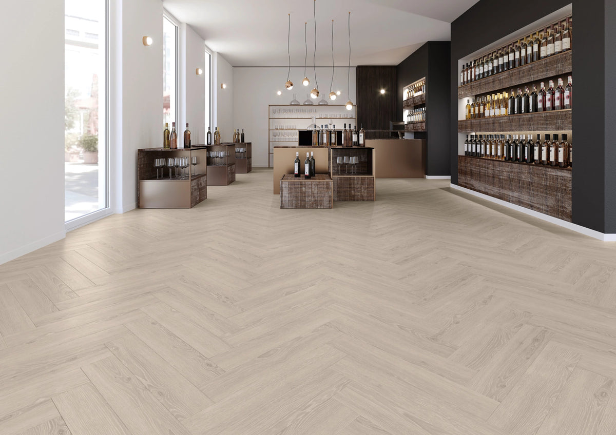 JOKA Design 555 Cycle Dryback 5383 Perfect Grey Oak Klebevinyl in einem hellen Verkaufsraum mit Fischgrätverlegung